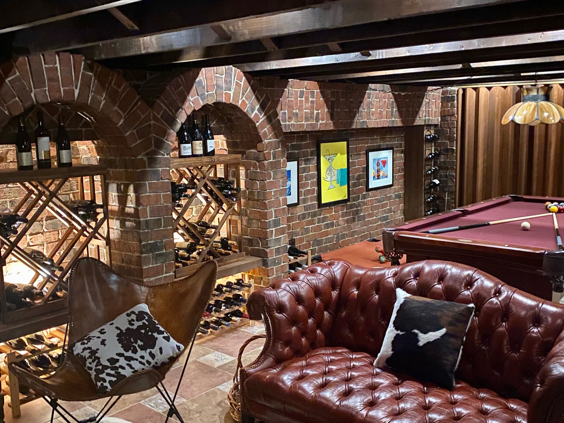 Wine cellar with brick arches, wine racks, leather seating, and a pool table.