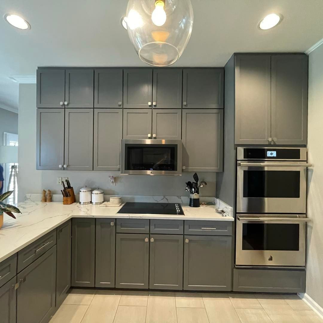 Gray kitchen cabinets and appliances with a white countertop and light wooden floor.