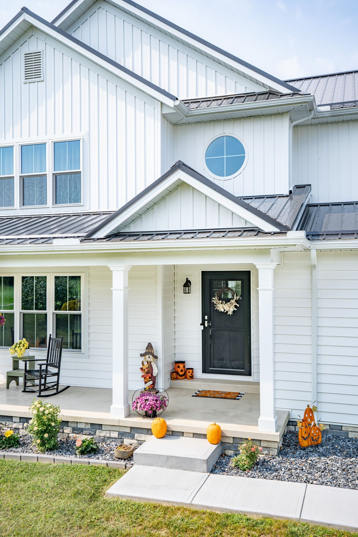White farmhouse with black door, porch, and pumpkins; fall decorations.