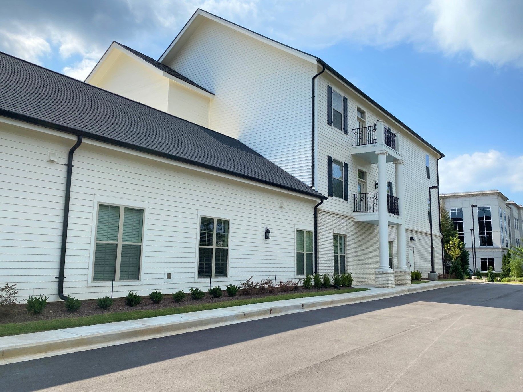 White multi-story building with black roof and shutters under a blue sky.
