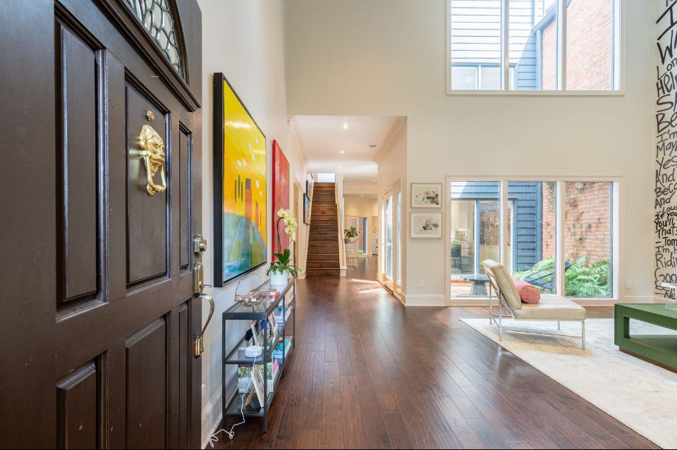 Dark brown front door opens into a modern home's entryway with wood floors, art, and a small sitting area.