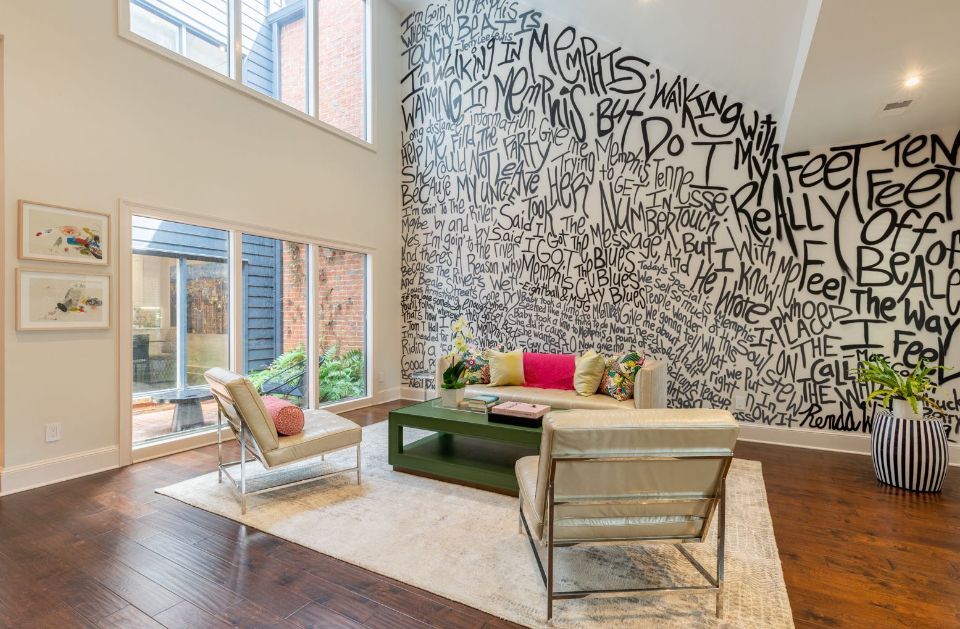 Living room with a graffiti wall, two chairs, a couch, a green coffee table, and a rug.
