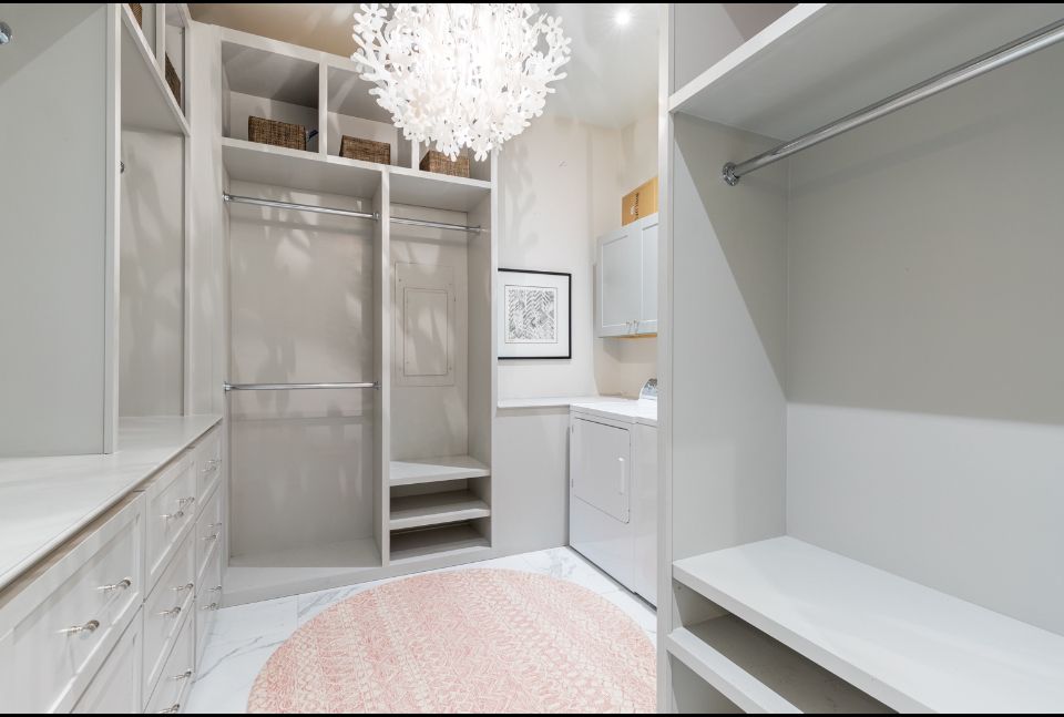 Walk-in closet with pale gray built-ins, laundry machine, pink rug, and chandelier.