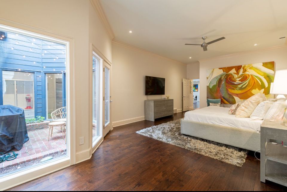 Bedroom with patio access, dark wood floors, large art piece, bed, TV, and side table.