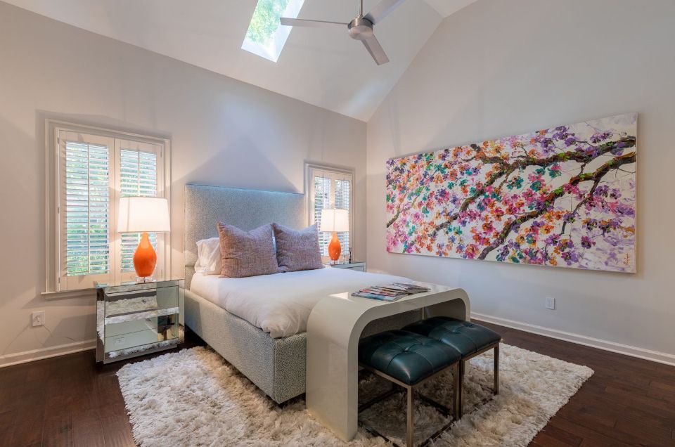 Bedroom with light blue upholstered headboard, white bedding, large floral artwork, and a white fluffy rug.
