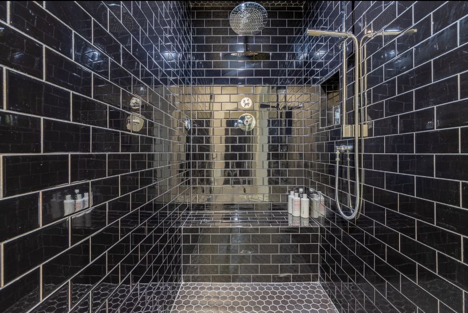 Dark tiled shower with glass door and rain showerhead.