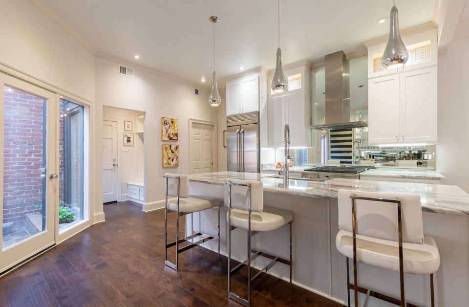 Modern kitchen with white cabinets, marble island, stainless steel appliances, and dark hardwood floors.