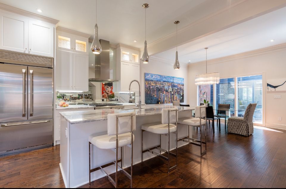 Modern kitchen with white cabinets, stainless steel appliances, island with stools, and dining area.