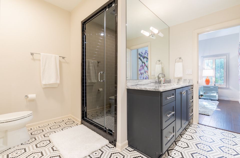 Modern bathroom with patterned tile, dark gray vanity, and glass shower.