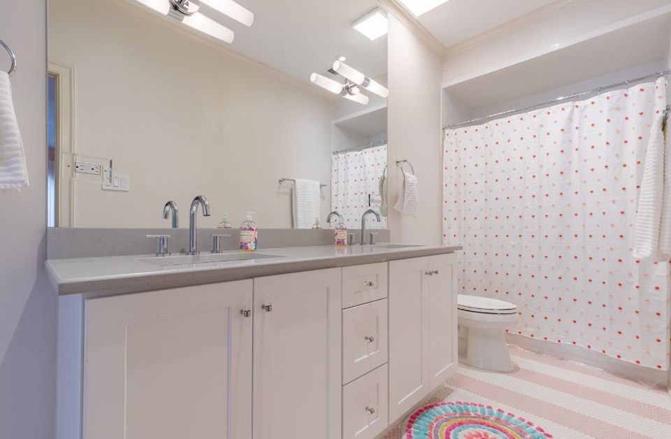 Bathroom with white cabinets, double sinks, large mirror, and polka dot shower curtain.