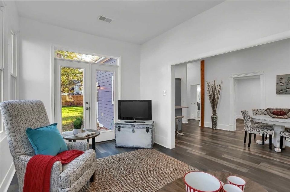 Living room with patterned armchair, TV on a trunk, and doorway to dining area, hardwood floors, natural light.