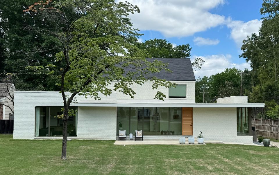 White modern house with large windows, wooden door, and a green lawn under a cloudy sky.