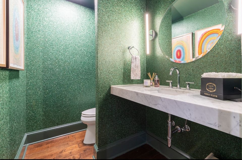 Green sparkly powder room with marble vanity, circular mirror, and artwork.