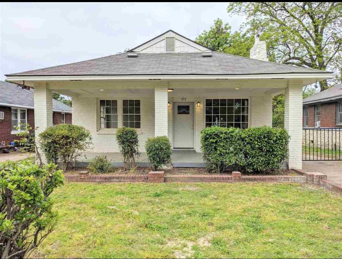 A one-story white house with a porch and green bushes in front.