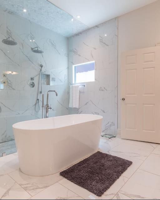 Luxurious white marble bathroom with a freestanding tub, shower, and small window.