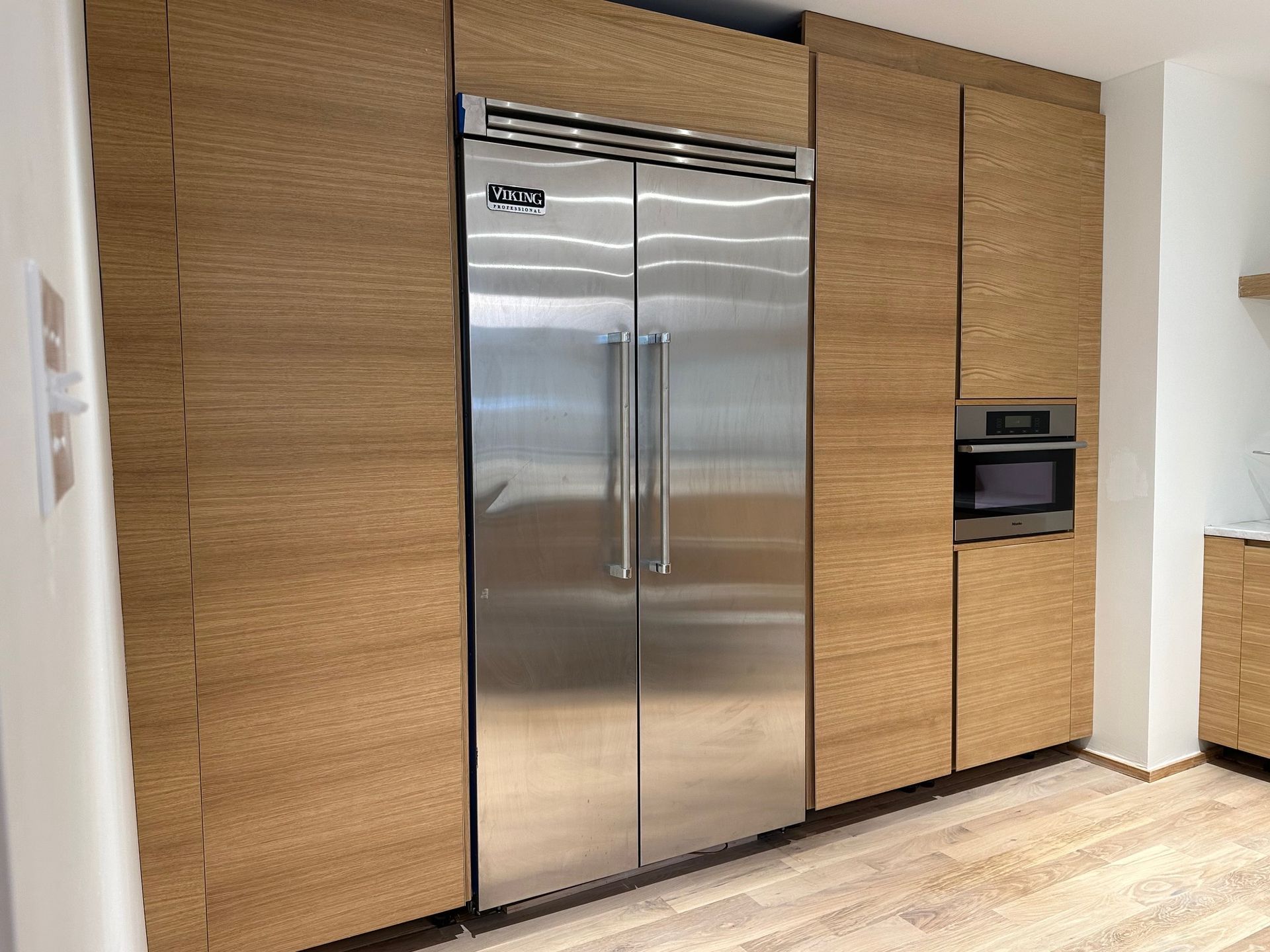 Stainless steel refrigerator and oven built into wood cabinetry in a kitchen.