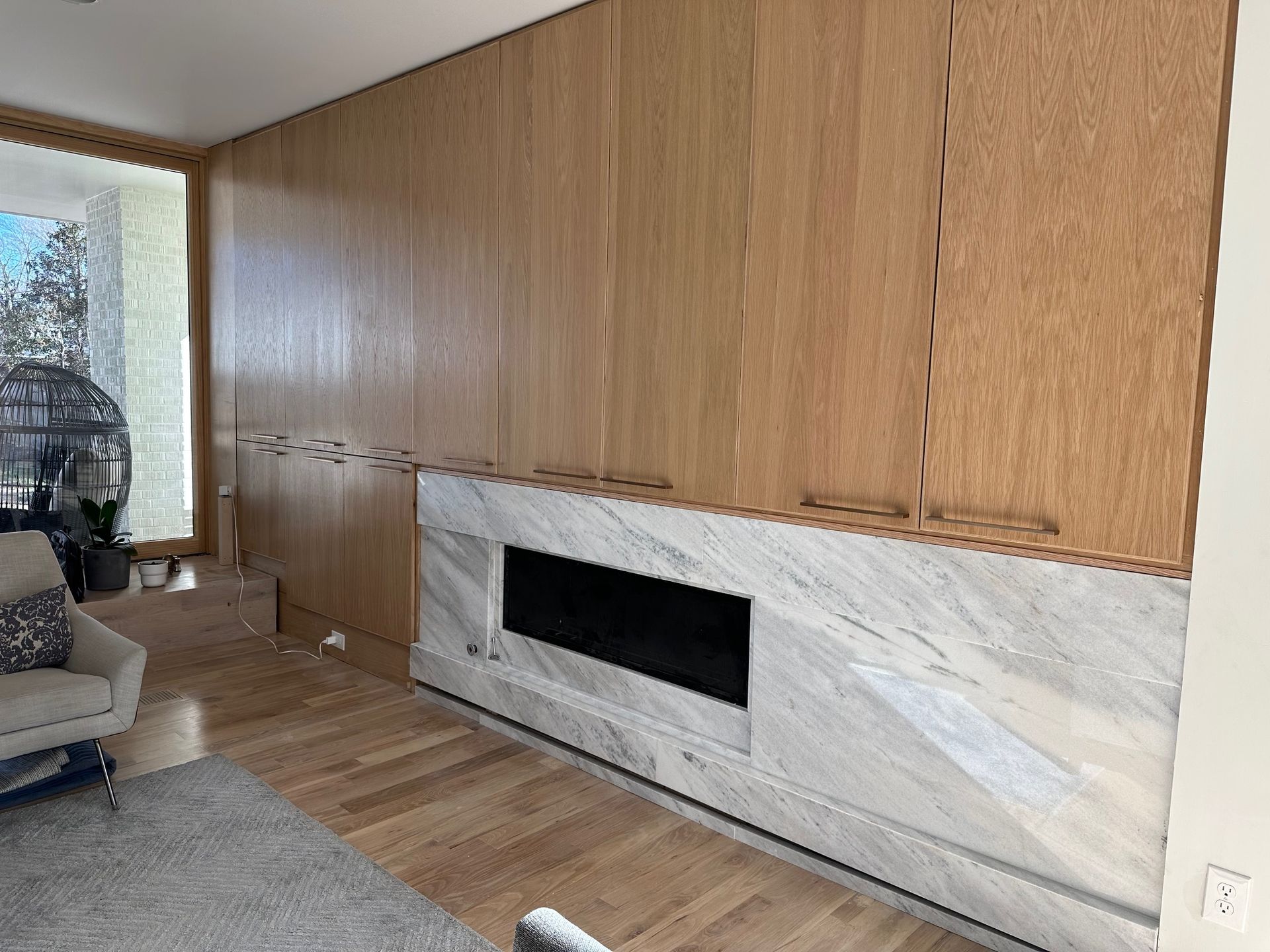 A fireplace with a marble facade set beneath wood-paneled wall storage.