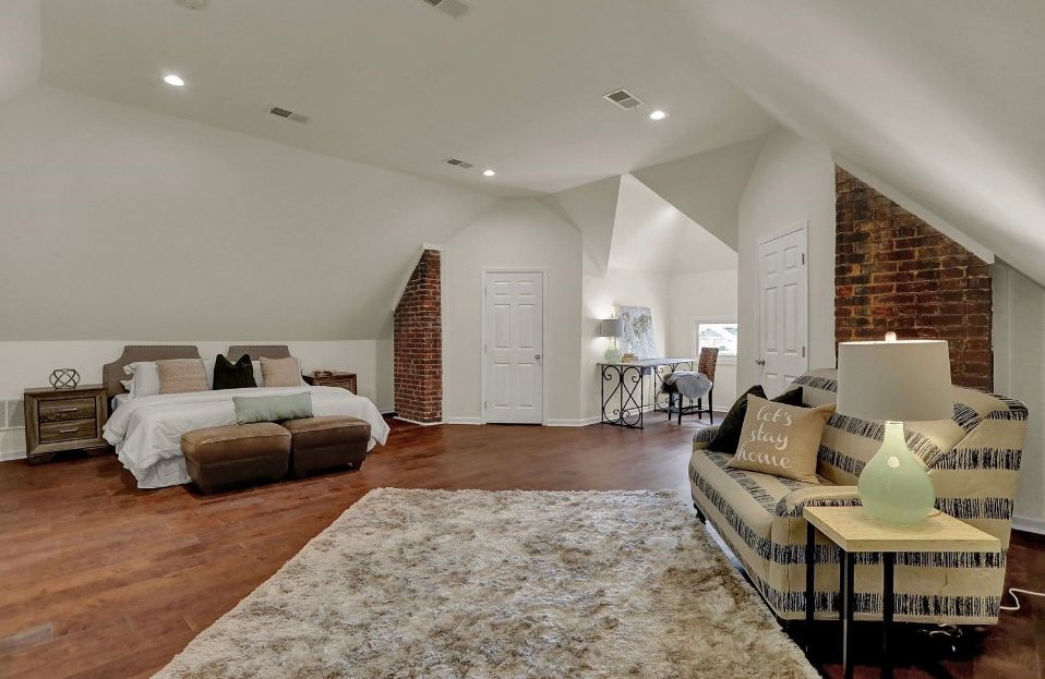 Spacious bedroom with a bed, sofa, and brick accent walls. The room has hardwood floors.