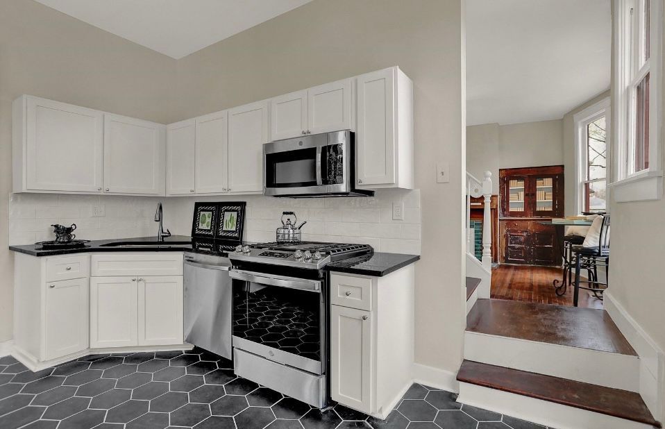 White kitchen with black countertops, stainless steel appliances, and dark hexagon tile floor.