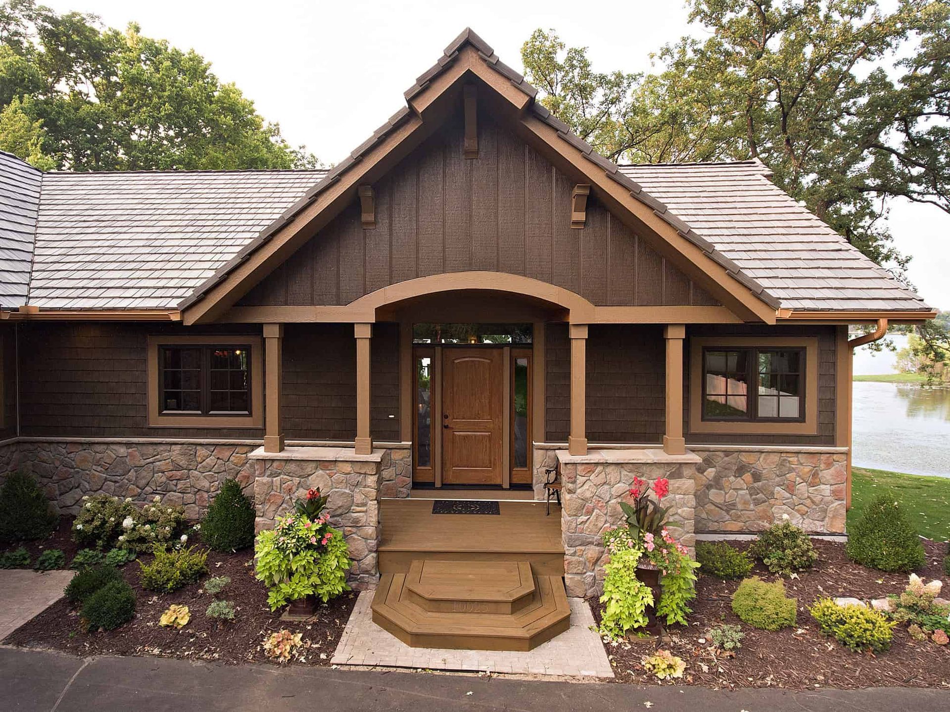 Rustic brown cabin with stone base, wooden door, and small front porch overlooking a lake.