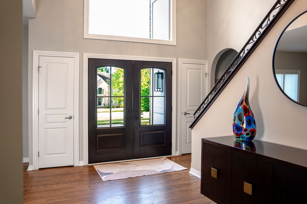 Entryway with double doors and stairs. Dark wood front door, light-colored walls, brown cabinet, and a large round mirror.