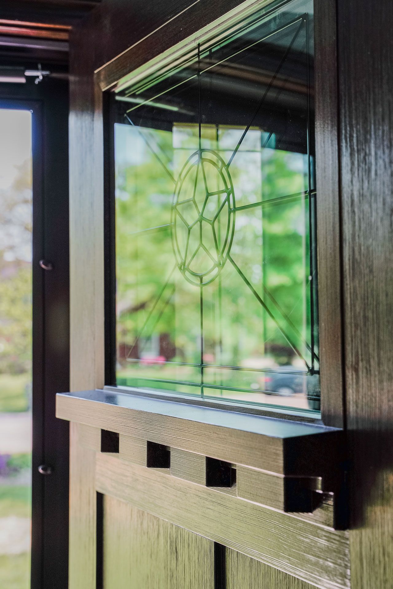 Stained glass window with geometric star design in a dark wood frame, set inside a Craftsman style interior.