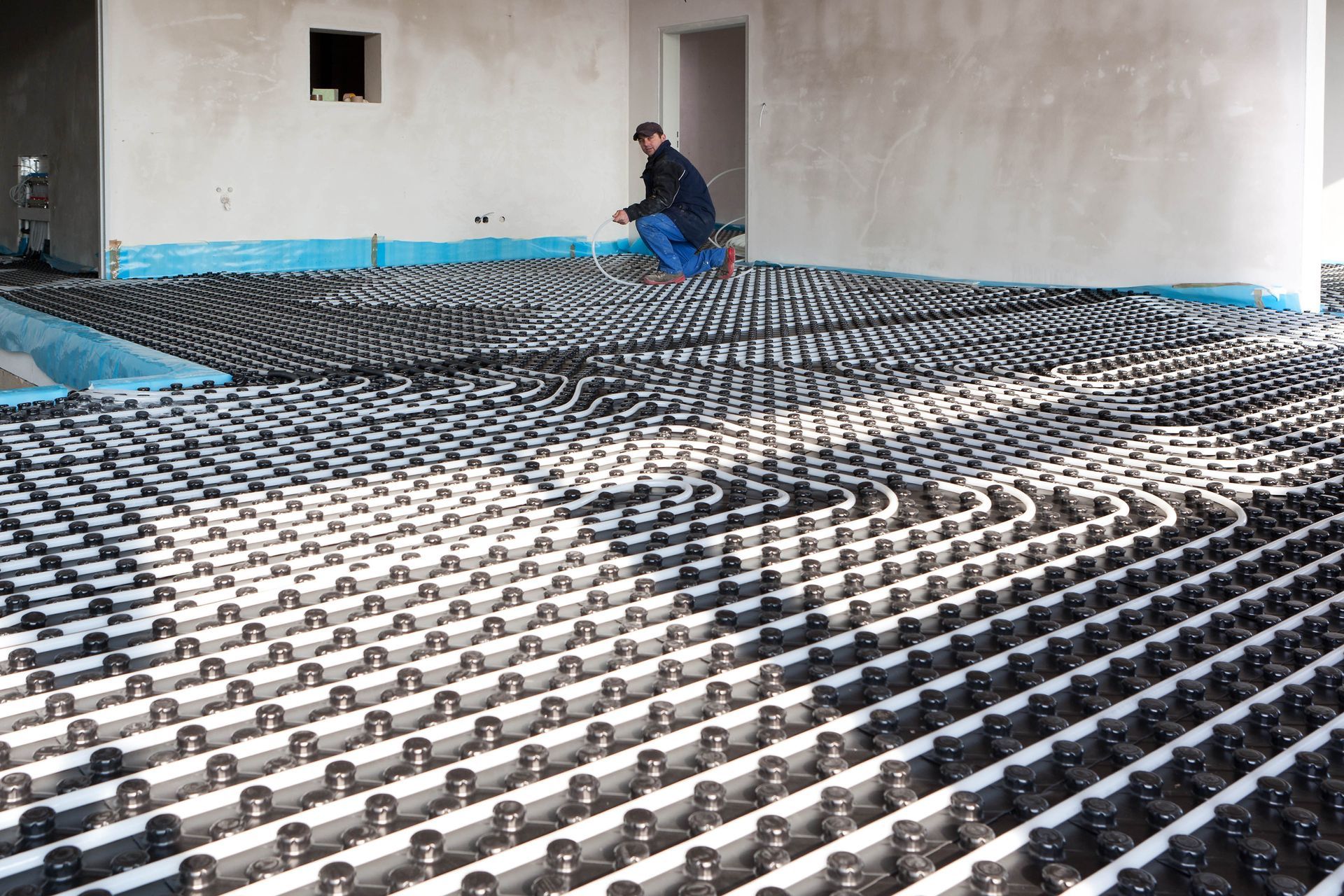 Man inspecting radiant floor heating system installation with black tubing and blue edging.