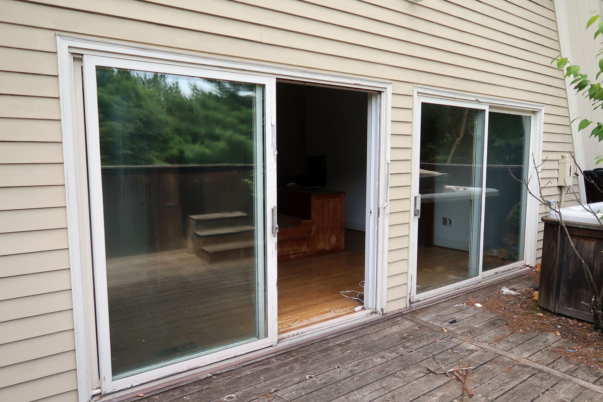 Sliding glass doors open onto a deck. The interior features stairs and furniture. The siding is beige.
