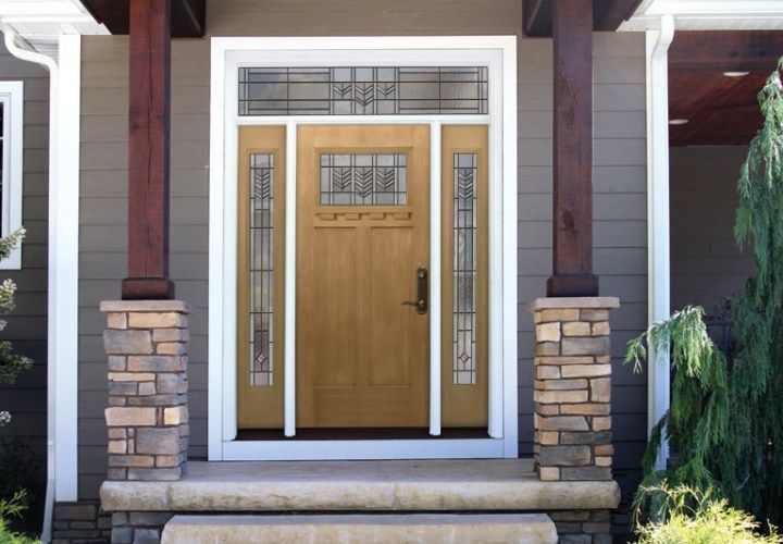 Beige front door with sidelights and transom, framed by white trim and supported by stone columns.