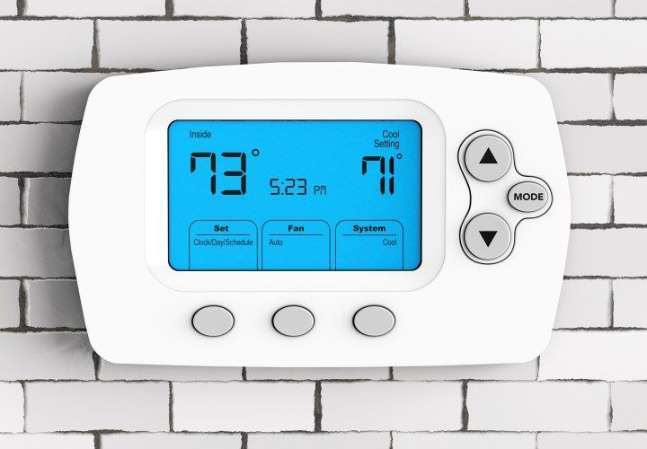 White digital thermostat showing 73 degrees inside, 71 degrees cooling set, mounted on a white brick wall.
