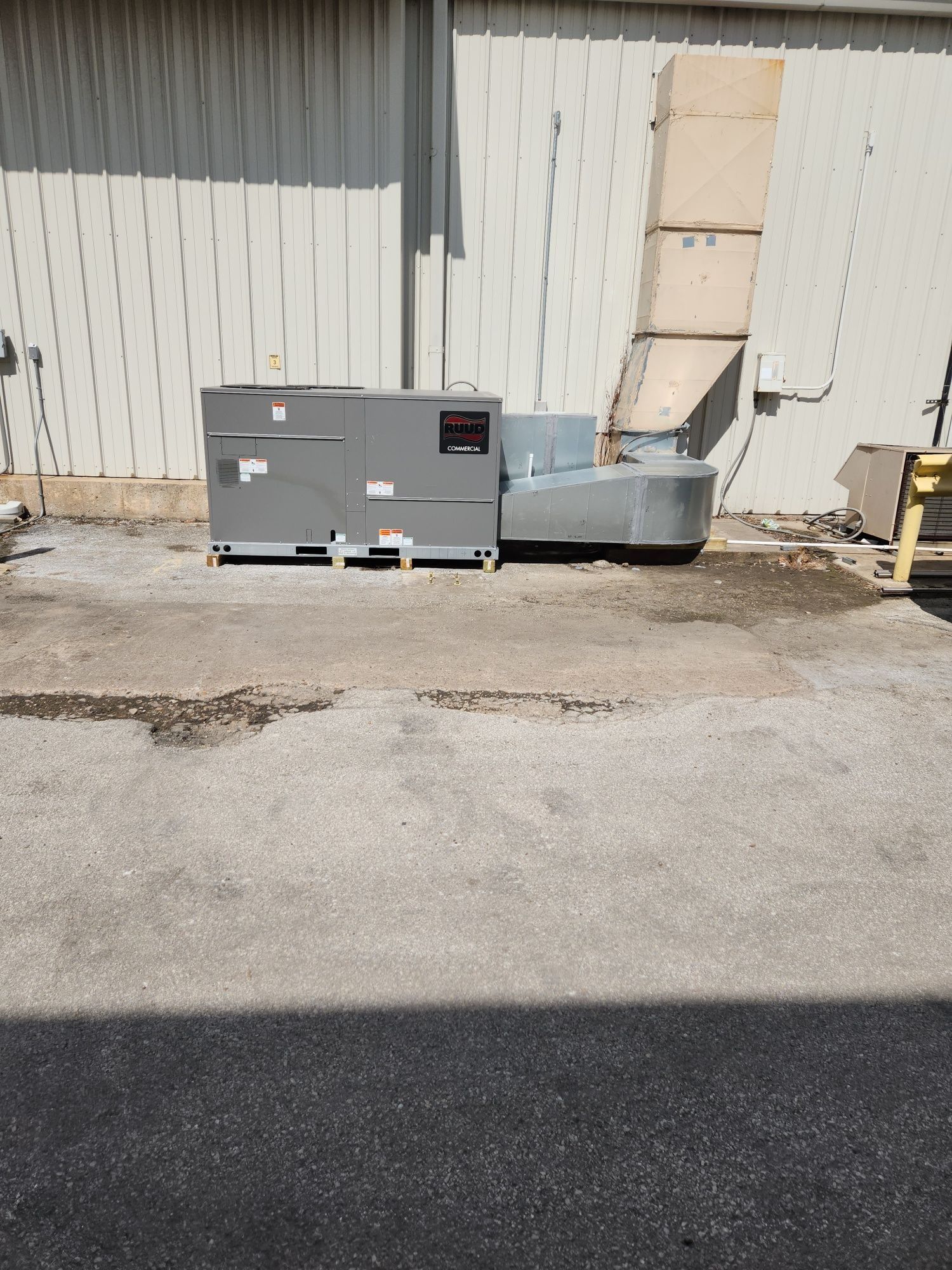 Gray HVAC unit with large ductwork beside a corrugated metal building and loading dock area