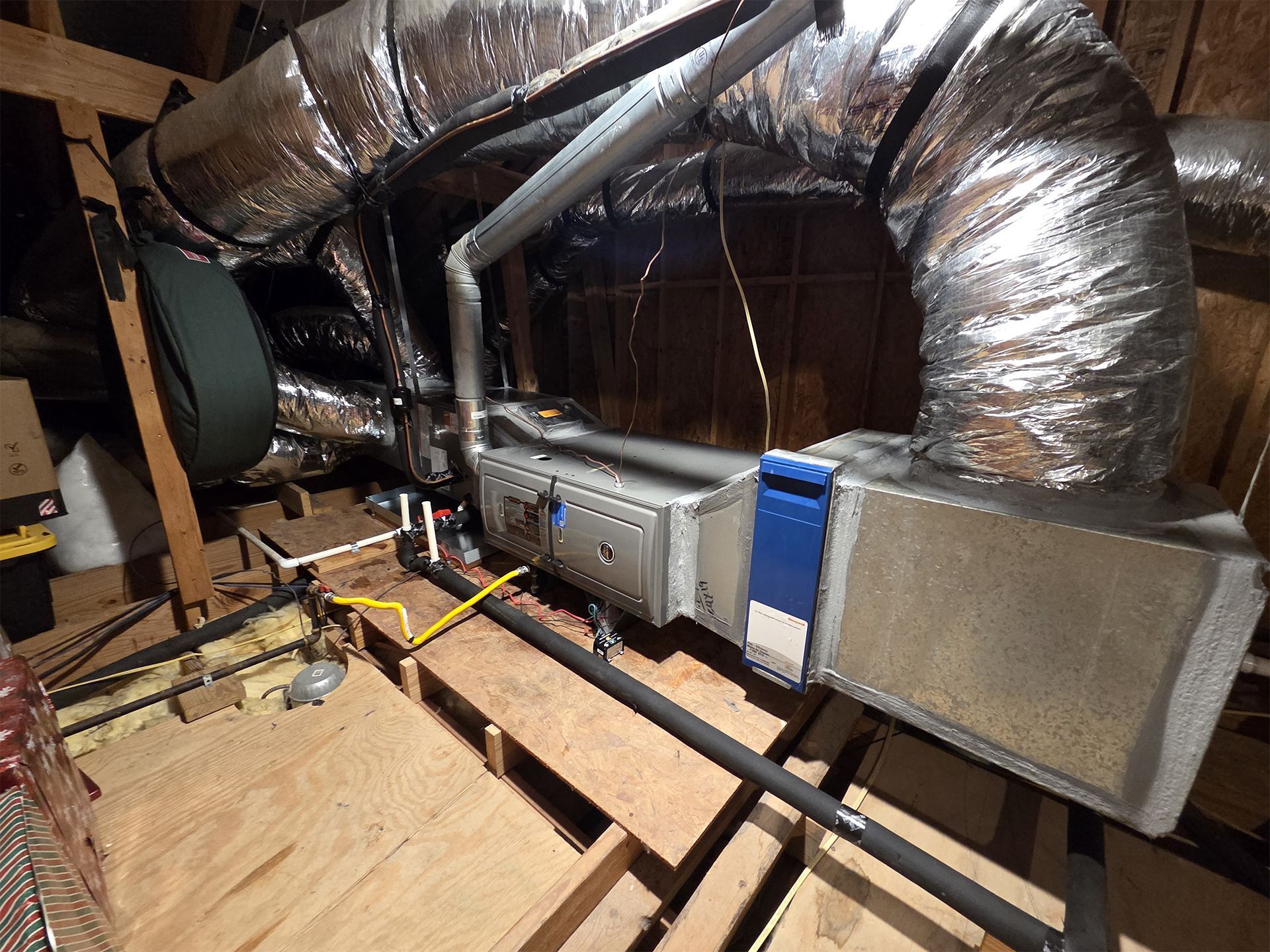 Attic HVAC ductwork with insulated silver ducts and metal furnace equipment over exposed wooden floor joists.