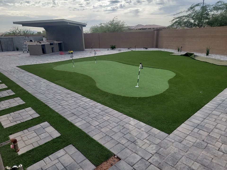 A backyard with a putting green and a brick walkway.