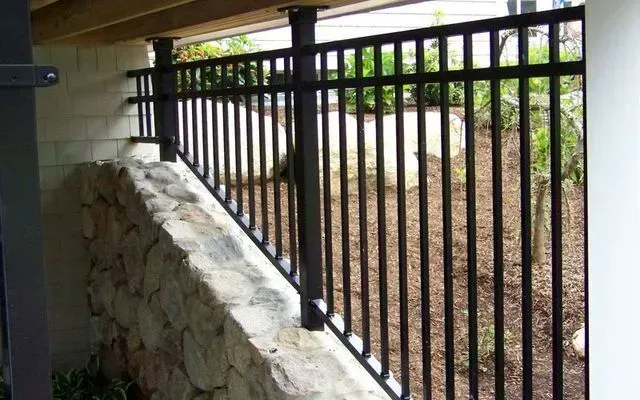 Black metal railing installed along the top of a stone retaining wall under a deck.