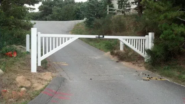 A white wooden gate blocking a paved road in a wooded setting.