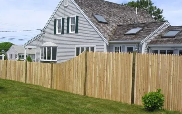 A gray house with a wooden picket fence in a grassy yard under a blue sky.