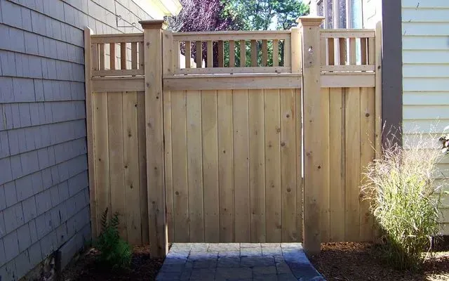 A wooden privacy gate with a decorative latticed top, situated between two sections of a matching cedar wood fence.