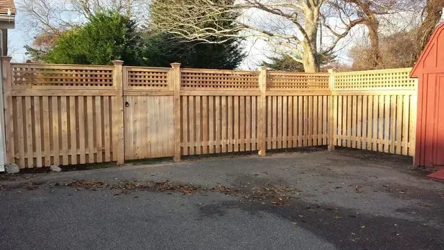 A new wooden picket fence with a lattice topper and a matching gate, set against a paved area and a red shed.
