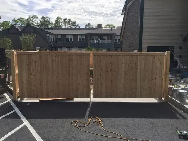 A pair of newly installed wooden gate panels standing on a parking lot surface in front of multi-family housing.