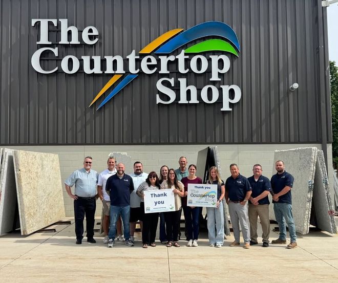Group of people standing outside The Countertop Shop holding signs in front of large stone slabs