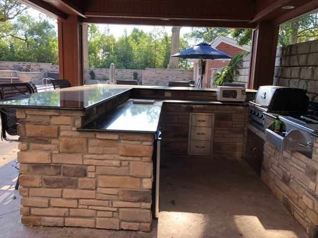 Outdoor kitchen with stone facade, dark countertop, and built-in grill.