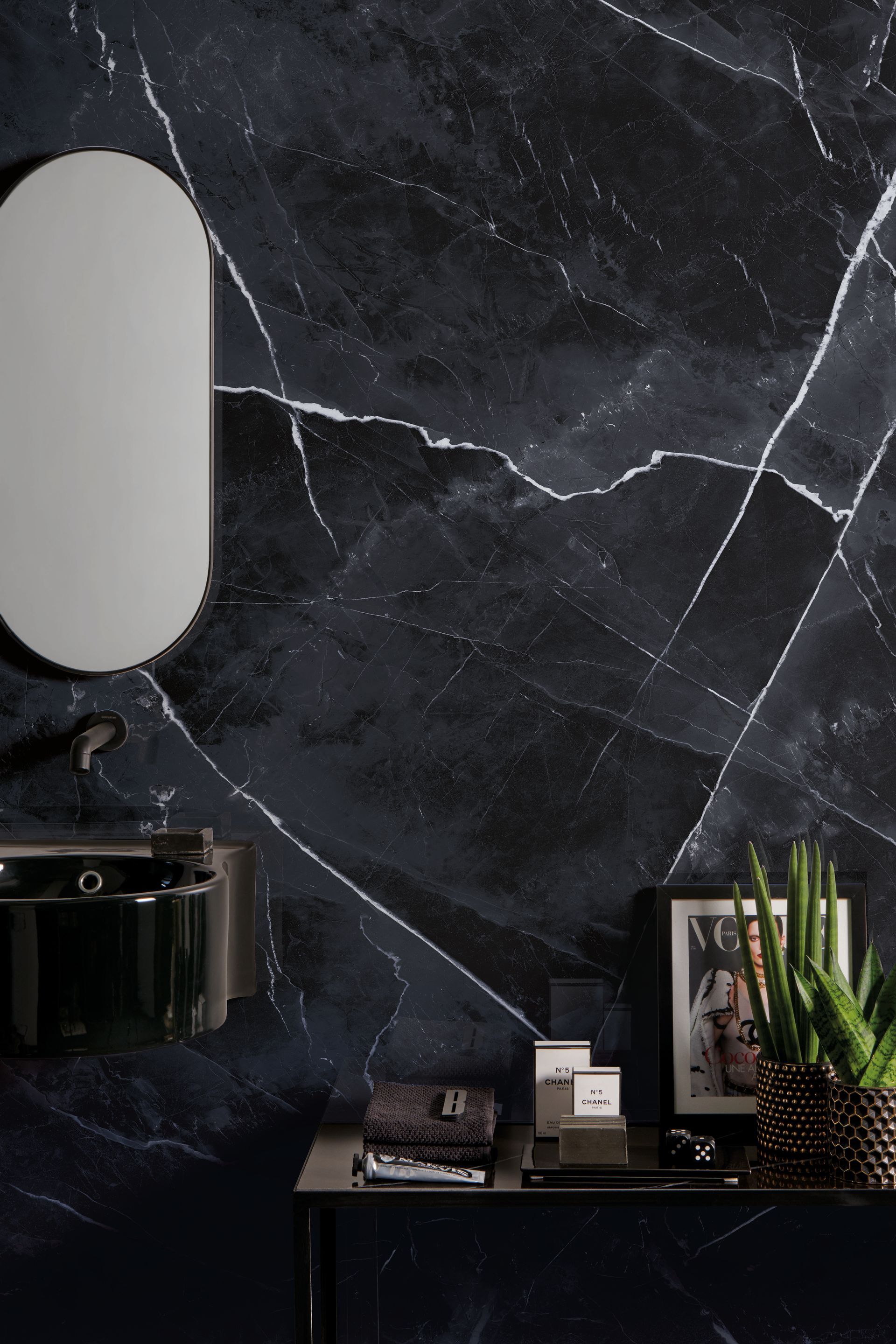 Modern interior with a dark marble wall, oval mirror, shelf decor, and a potted plant