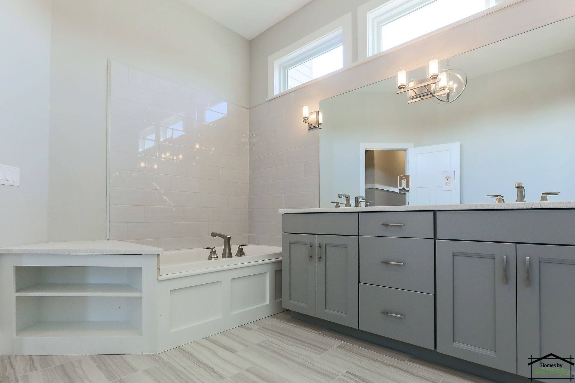 Modern bathroom with gray cabinets, white tile, tub, and large mirror.