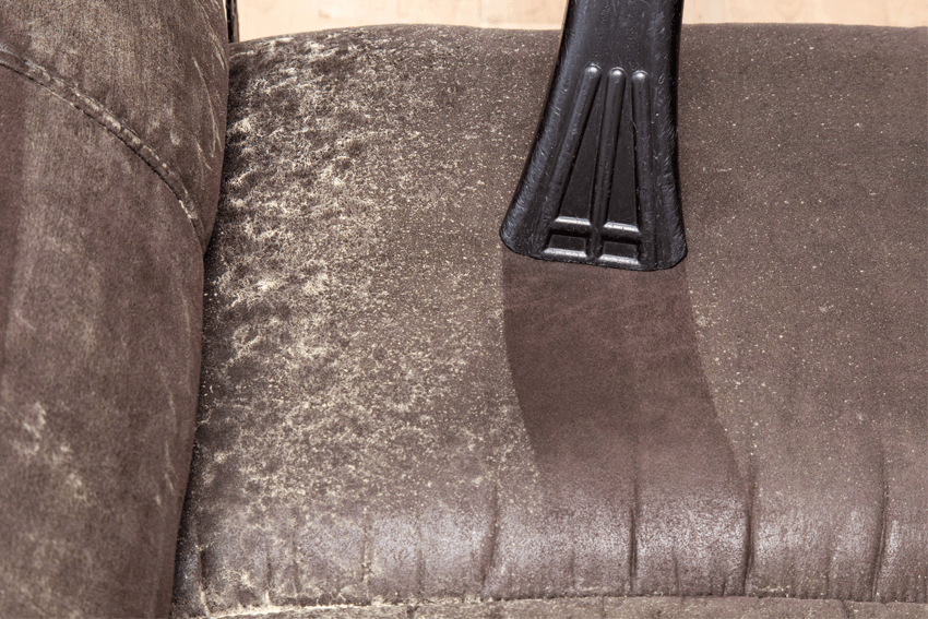 Vacuuming a brown leather couch; one side is dusty, the other is clean.