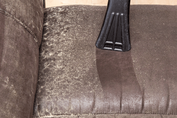 Vacuuming a brown leather couch; one side is dusty, the other is clean.