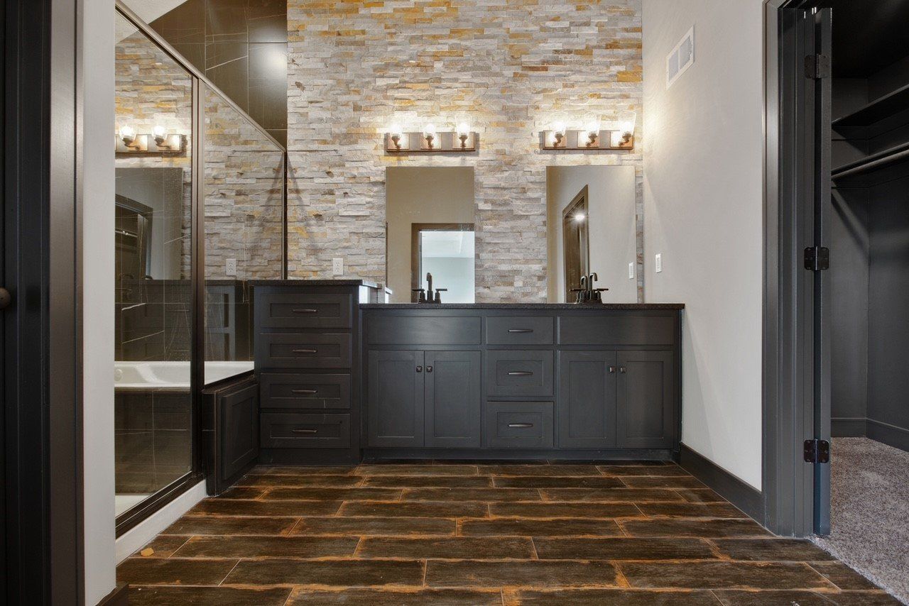 A bathroom with two sinks , a tub , and a brick wall.
