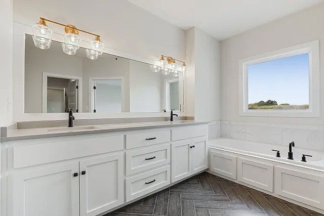 A bathroom with two sinks , a tub , and a window.