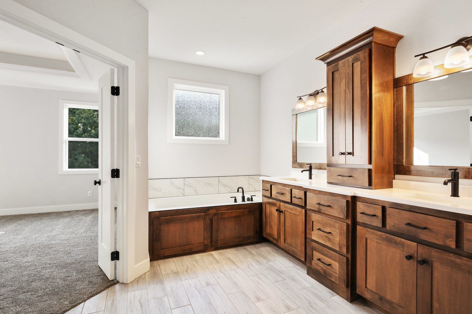 A bathroom with two sinks , a tub , and a mirror.