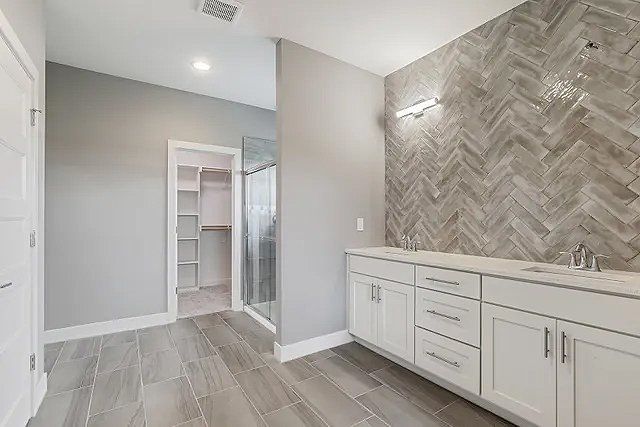 A bathroom with two sinks , a walk in closet and a shower.