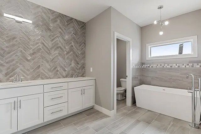 A bathroom with two sinks , a tub , a toilet and a window.